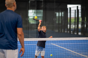 Coach teaching padel to child student on court